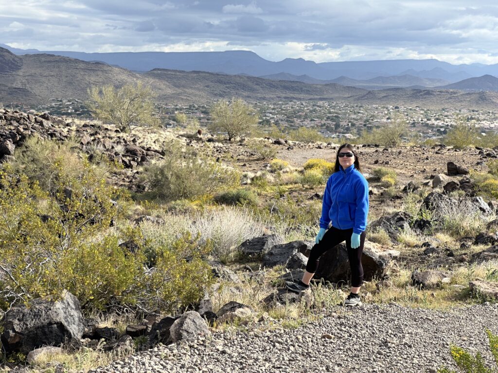 image of the author from the 'About Me,'section of the blog. She is standing in a desert landscape with a scenic view of rugged terrain and distant mountains in the background. 