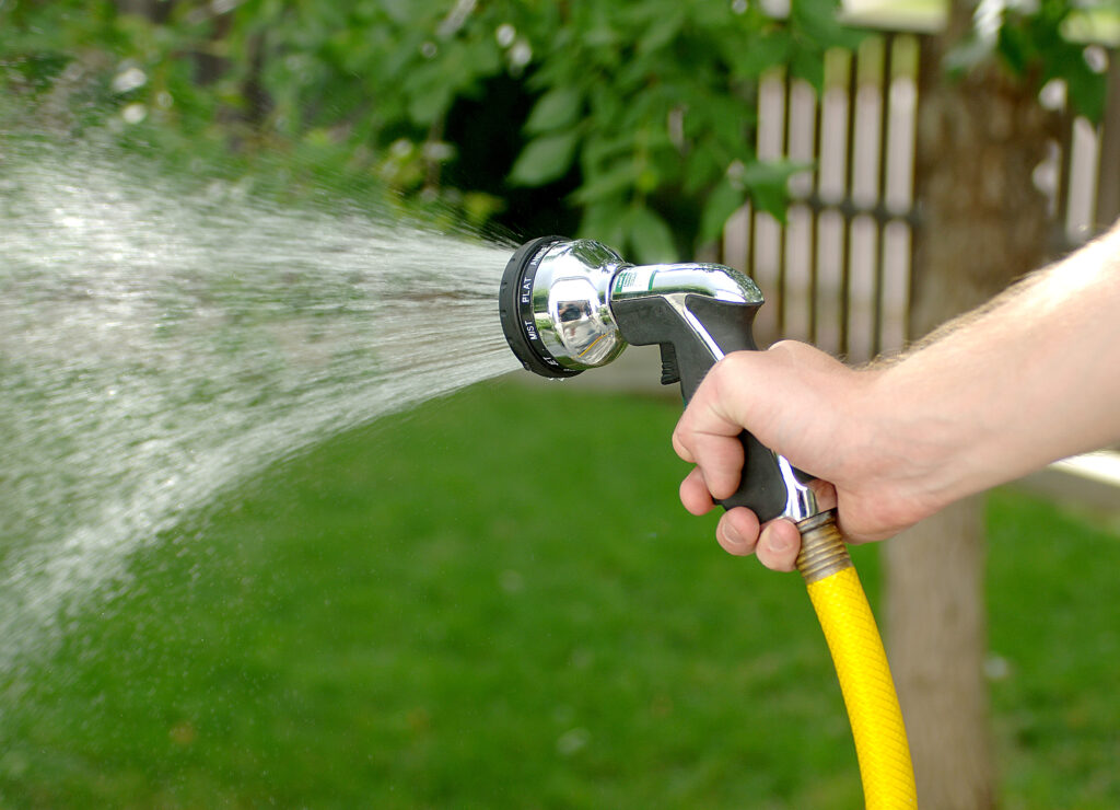 a yellow hose with a metal nozzle with water coming out of it. A person's hand is holding it.